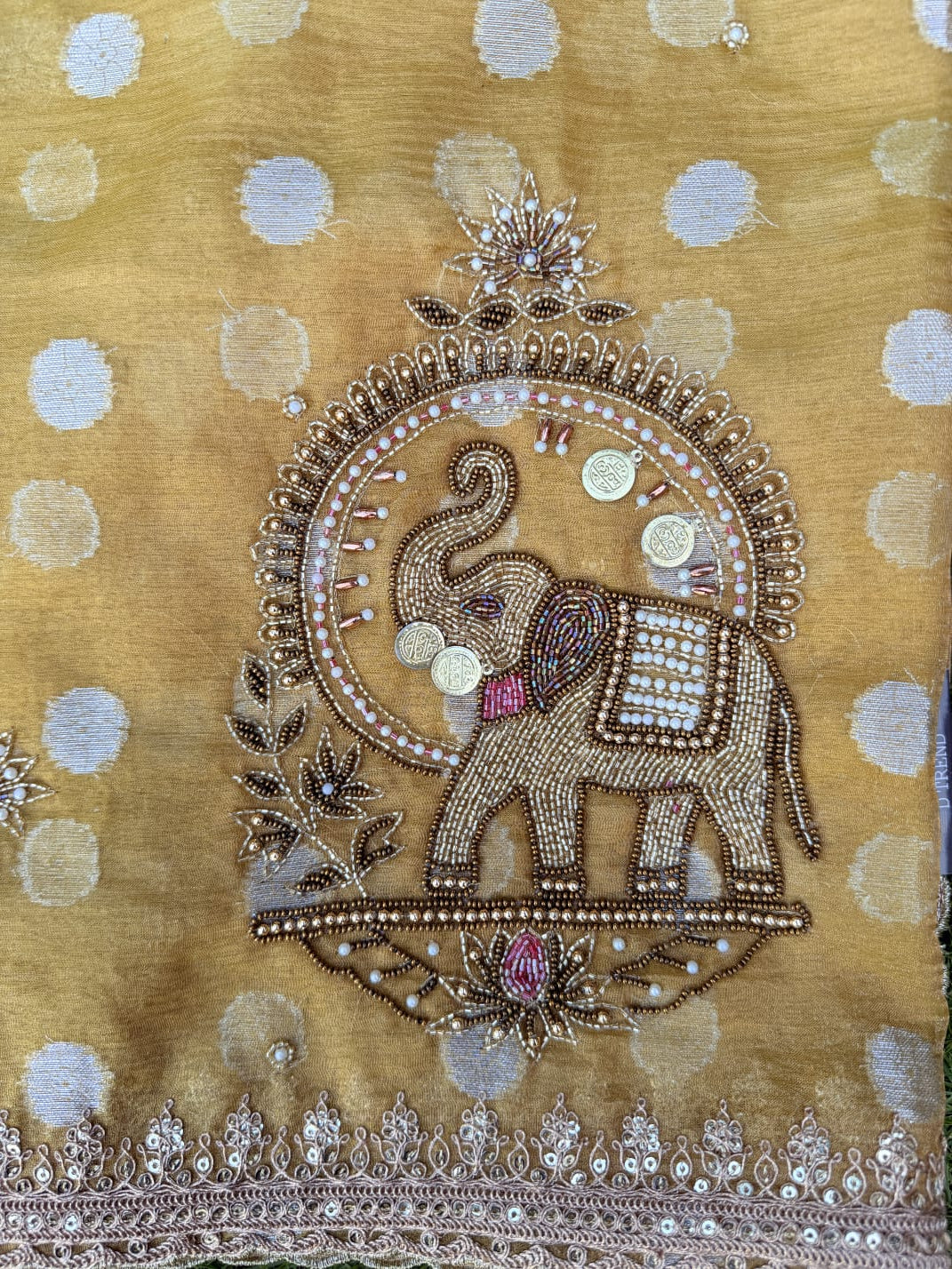 Close-up of beaded elephant embroidery with floral accents and scalloped border on a mustard yellow organza saree.