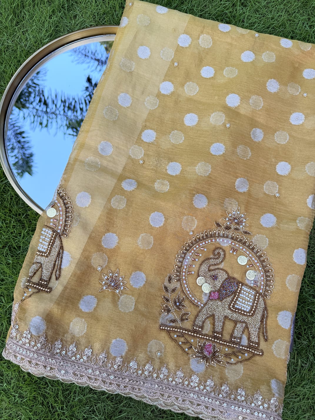 Mustard yellow organza saree with embroidered elephant motifs, dotted detailing and a decorative cutwork border, close-up.