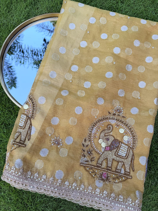 Mustard yellow organza saree with embroidered elephant motifs, dotted detailing and a decorative cutwork border, close-up.